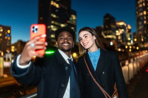 Diverse couple smiling, taking a selfie outdoors in an urban environment at night, capturing a