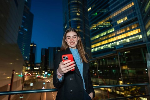 Young woman smiling while reading content on her red smartphone, enjoying digital communication and