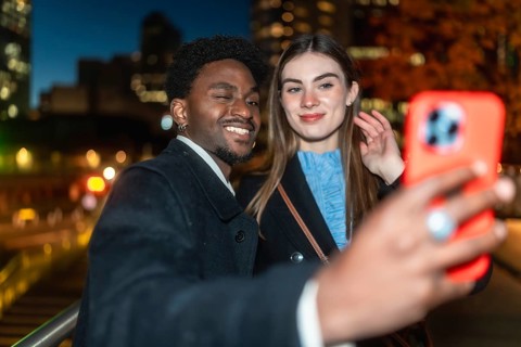 Diverse young couple on a city street at night, smiling and taking a candid selfie with a