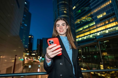Young woman smiling and holding a smartphone, capturing a selfie or video while standing on a