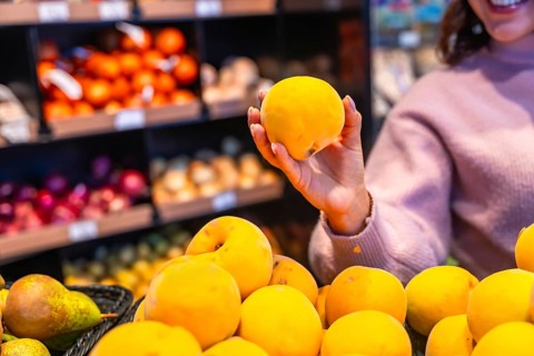 Woman selecting a ripe peach from the fresh produce section, highlighting healthy eating choices