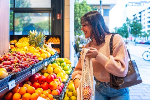 Smiling woman browsing and selecting fresh organic fruit from a display stand in a modern