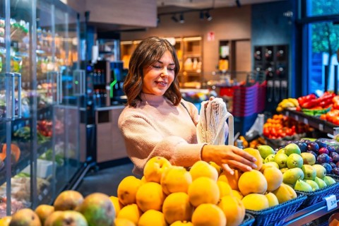 Woman choosing fresh organic produce from a display while shopping for groceries in a modern