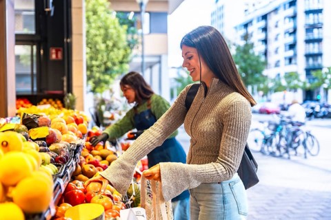 Smiling woman choosing fresh organic fruit and vegetables at an outdoor market stall, embracing a