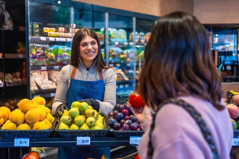 Smiling woman greengrocer assisting a customer choosing fresh organic fruit, including pears,