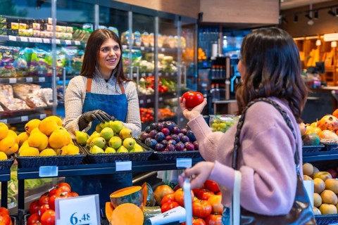 Friendly store employee warmly assisting a female customer selecting fresh organic produce at the