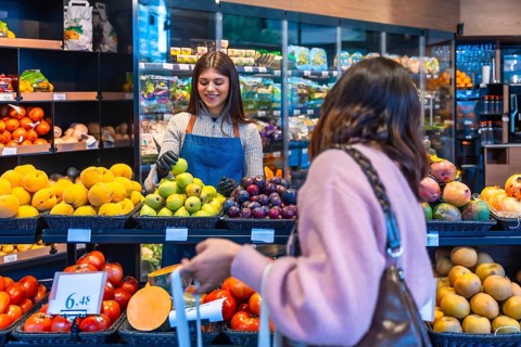 Friendly supermarket employee wearing an apron and gloves assisting a female customer in the