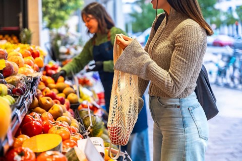 Woman holding a reusable mesh bag filled with fresh produce while shopping for organic fruits and