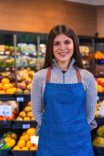 Young woman wearing a denim apron and a sweater, smiling confidently while standing in a