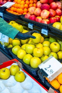 Hand in black protective glove selecting a fresh golden apple from a display of fruits and