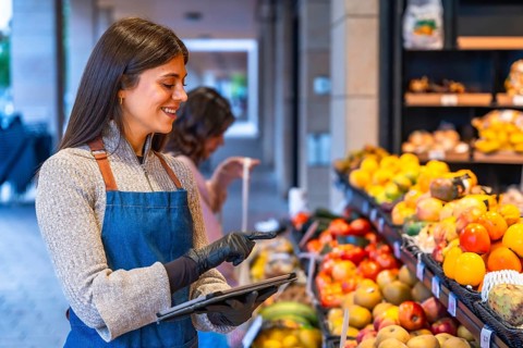 Female shop assistant wearing an apron and gloves managing fresh fruit and vegetables inventory
