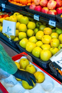 Person wearing a black glove carefully choosing ripe yellow apples from a display case at the fresh