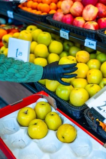 Person's hand, wearing a black protective glove, selecting fresh golden delicious apples from a