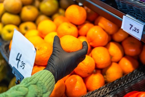 Person wearing a protective glove picking an orange from a large display of citrus fruits in a