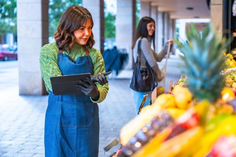 Female small business owner wearing an apron and gloves managing inventory and sales on a digital