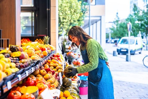 Woman smiling as she arranges colorful fresh fruits and vegetables on an outdoor market stand,