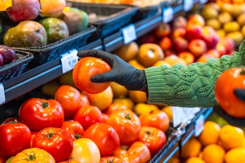Person wearing a protective rubber glove selecting a ripe tomato from a produce display at a