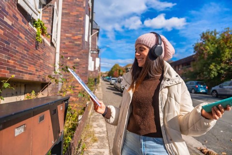 Happy young woman standing on an urban street, opening a mailbox to retrieve mail while wearing
