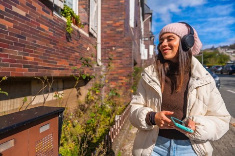 Young woman smiling and listening to music through headphones while walking outdoors on an urban