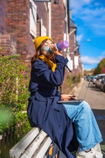 Woman hydrating with a water bottle while working remotely on her laptop, sitting on a bench in an