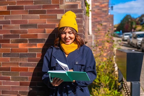 Young woman dressed in a trench coat and yellow beanie enjoying journaling and creative writing in