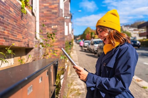 Young smiling woman wearing a yellow beanie and blue trench coat showing excitement finding a