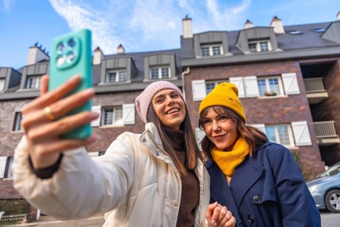 Two young women friends enjoying a fun moment together, smiling and taking a selfie outdoors in a