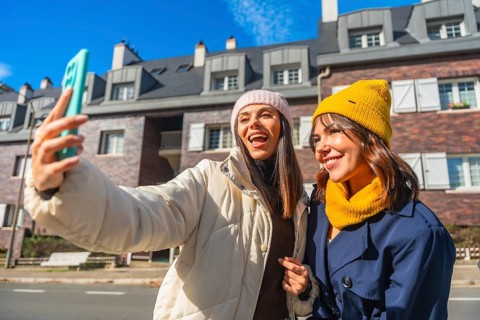 Two cheerful young women friends are enjoying a sunny winter day in the city, smiling and taking a