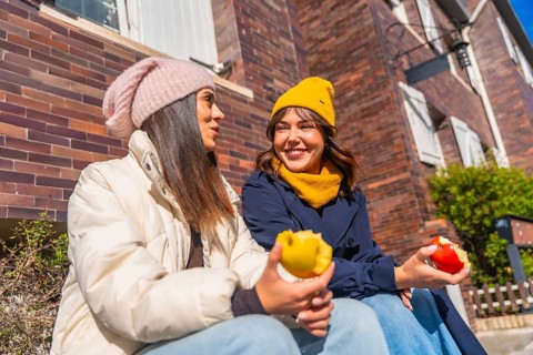 Two young women friends sitting together on a sunny autumn day, enjoying fresh apples while having