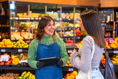 Grocery store employee with a tablet providing excellent customer service and smiling while talking