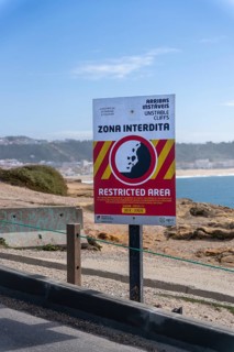 Sign with a warning about the cliff edge, Farol de Nazare, Portugal