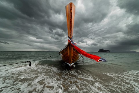 Longtail boat on the beach with dark rain clouds behind it, Koh Ngai island, Andaman Sea, Satun
