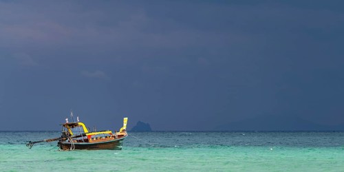 Longtail boat (Thai: Ruea Hang Yao) on the beach, behind it an approaching thunderstorm, Koh Ngai