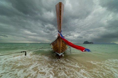 Longtail boat on the beach with dark rain clouds behind it, Koh Ngai island, Andaman Sea, Satun