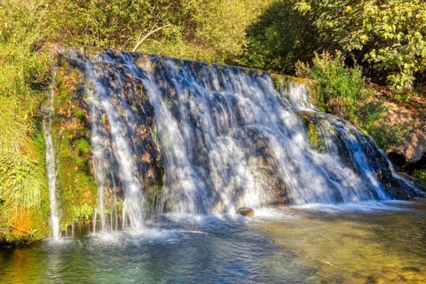 Fascinating waterfall flowing over green moss rocks into a natural basin, El Kelaa wild stream in