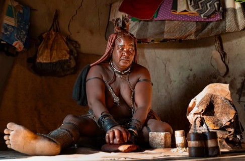 Elderly Himba woman making red paste for skin care, in a hut, traditional Himba village, Kaokoveld,