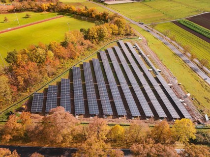 Solar systems next to a sports field, surrounded by autumn-colored trees, Bau PV Freifaechenanlage,
