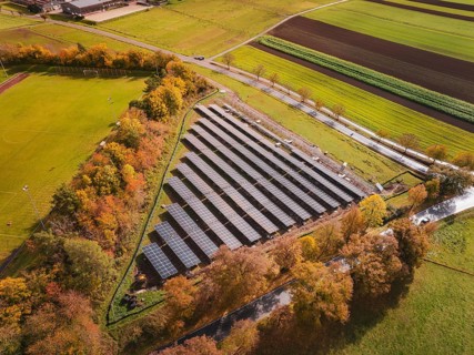Aerial view of solar panels surrounded by autumn trees and green fields, Bau PV Freifaechenanlage,
