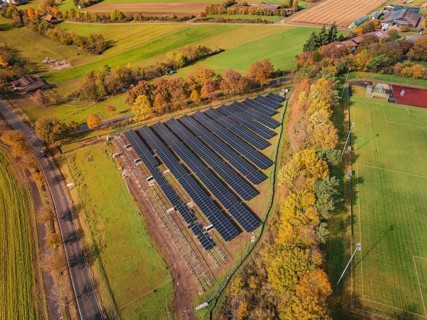 Aerial view of a solar field in an autumn landscape with fields and colorful trees, PV