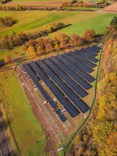 Panoramic aerial view of a solar plant surrounded by green fields and autumn trees, PV open-air