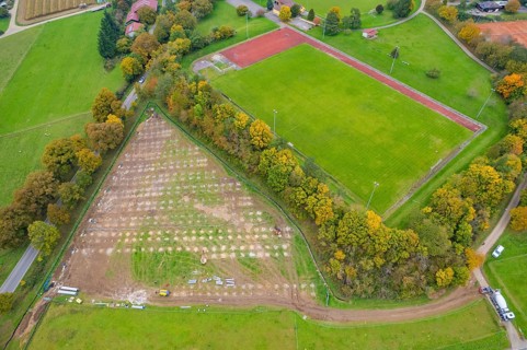 Aerial view of a sports field next to a large field and surrounded by autumn trees, PV