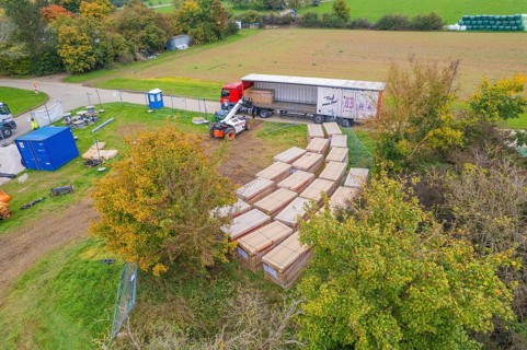 A forklift truck moves boxes next to a truck in a green autumn landscape, Bau PV Freifaechenanlage,