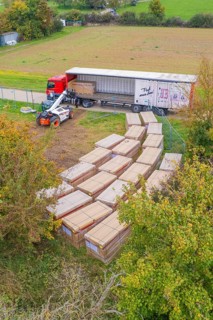 Aerial view of a forklift truck working next to a truck with boxes and autumn trees, PV