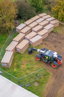 A forklift truck arranges stacked boxes on a fenced meadow in autumn, Bau PV Freifaechenanlage,