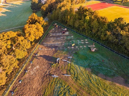 Construction site next to a sports field, surrounded by trees and shade, illuminated by morning
