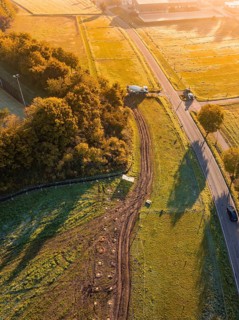 Road through fields with construction, surrounded by trees in early sunlight, construction PV