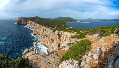 Tourist enjoying the view of steep cliffs by the sea, coastal landscape, cliffs on the Capo Caccia