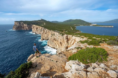 Tourist enjoying the view of steep cliffs by the sea, coastal landscape, cliffs on the Capo Caccia