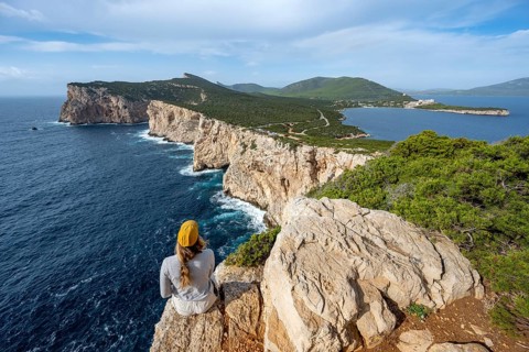 Tourist sitting on the edge of a steep cliff, view of steep cliffs by the sea, coastal landscape,