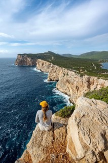 Tourist sitting on the edge of a steep cliff, view of steep cliffs by the sea, coastal landscape,